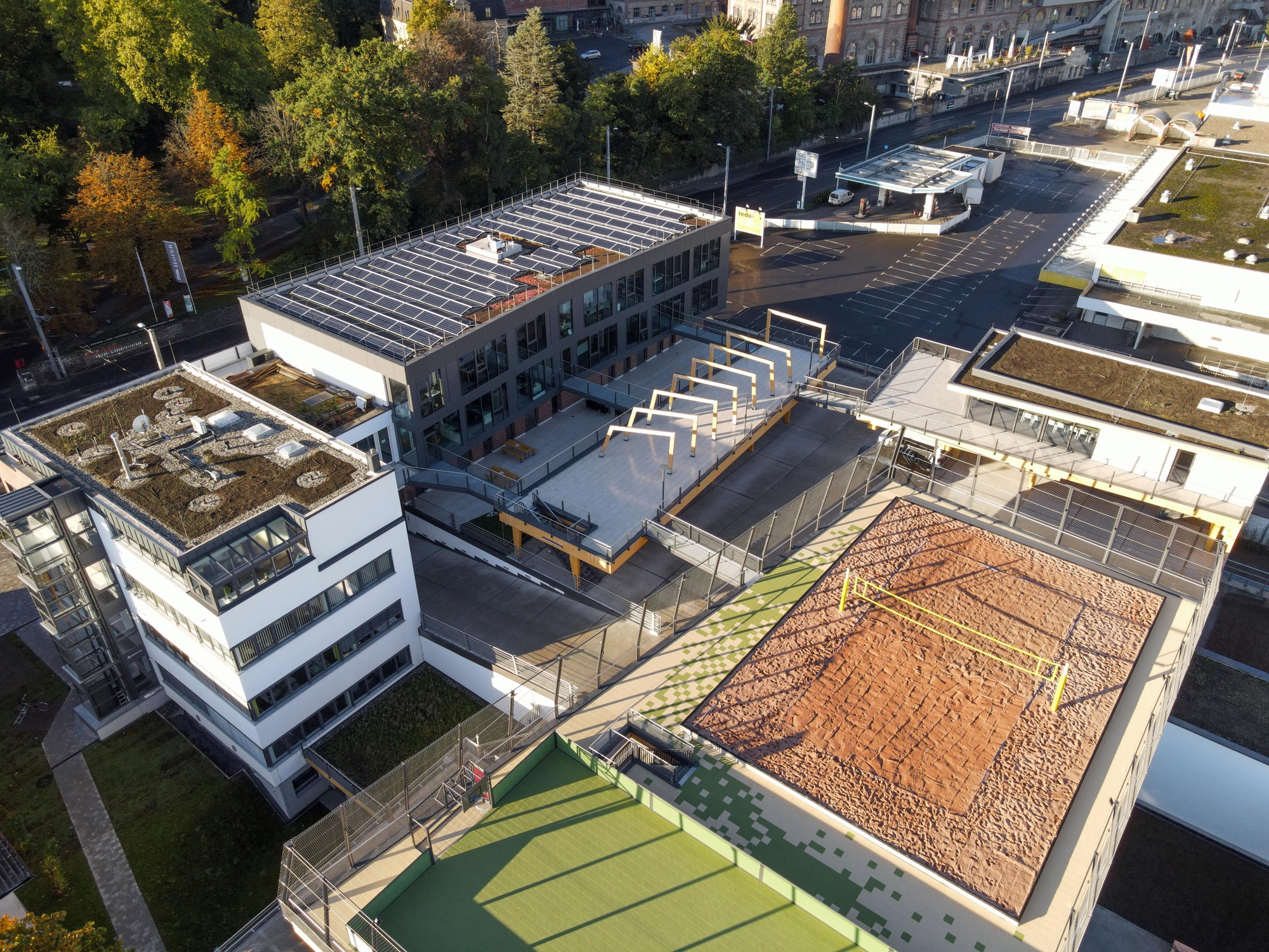 Luftaufnahme des Gebäudes Beach- und Businesscampus in Würzburg, welches vielfältige Dachflächen zeigt, wie ein Beach-Volleyball-Feld oder Photovoltaik-Anlagen